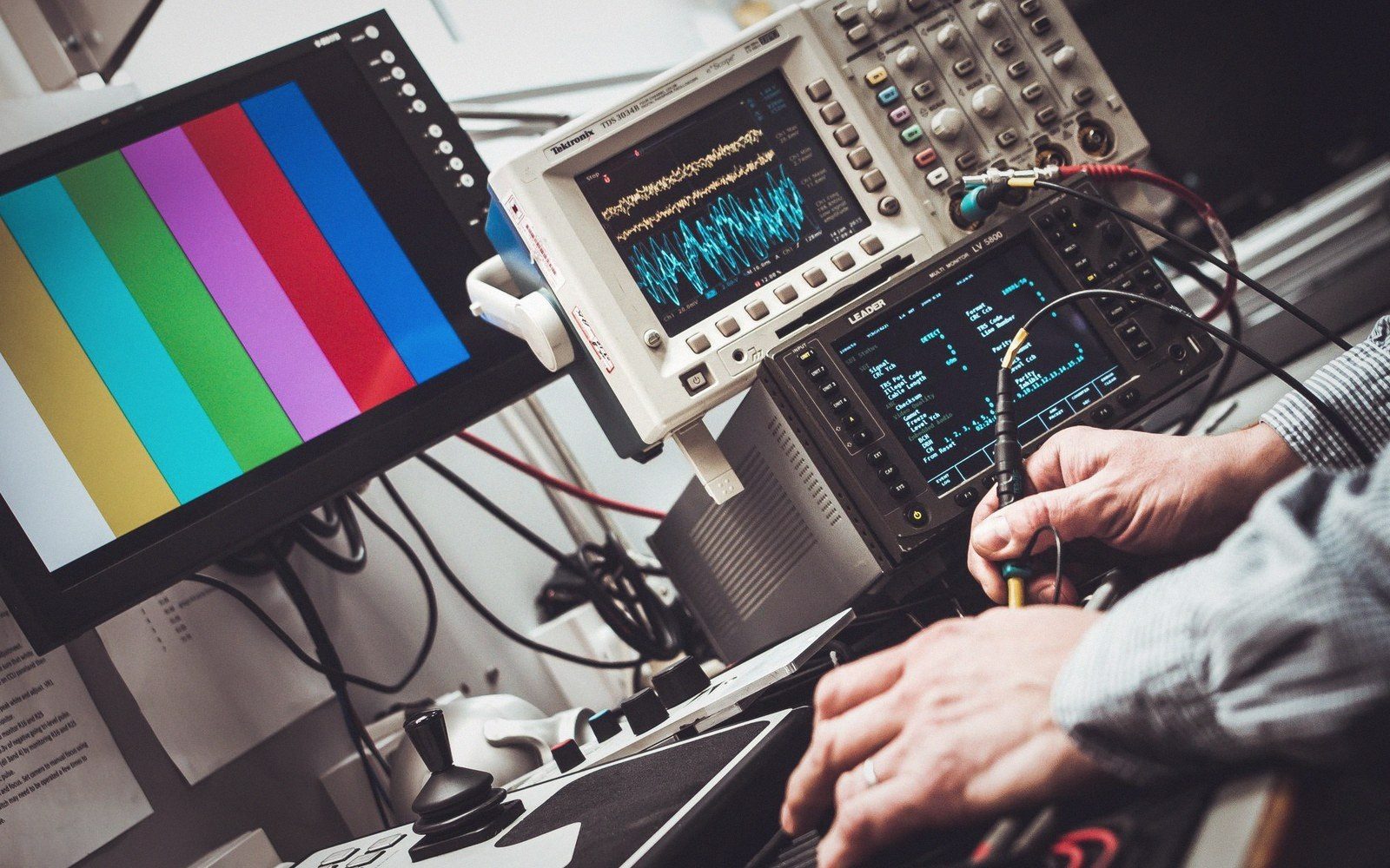 Technician adjusts an oscilloscope beside a color bar test pattern monitor